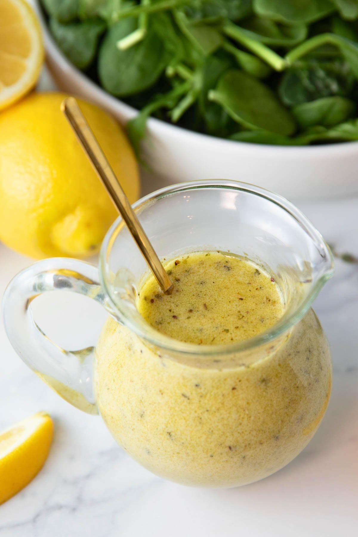 Jar of lemon vinaigrette dressing with bowl of spinach and lemons sitting in background