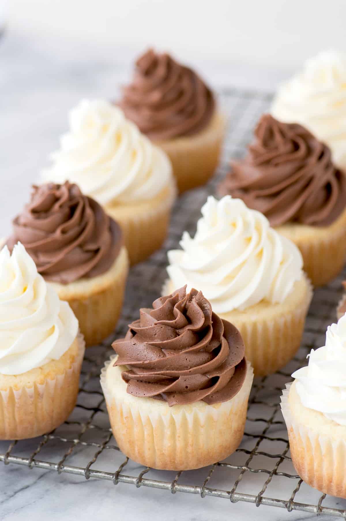 vanilla cupcakes with chocolate and white frosting on metal cooling rack on marble background