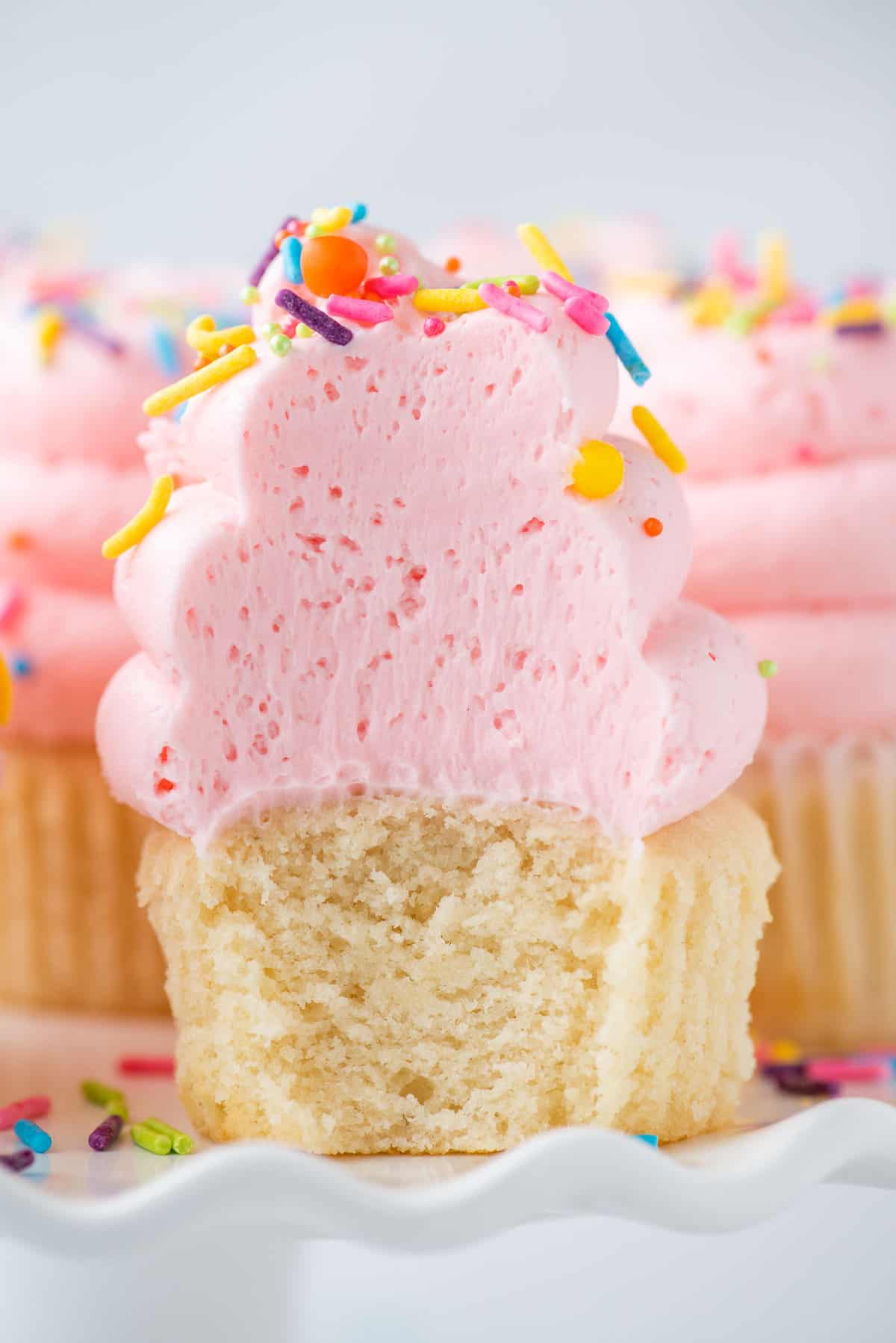 bite removed from vanilla cupcakes with pink frosting and sprinkles